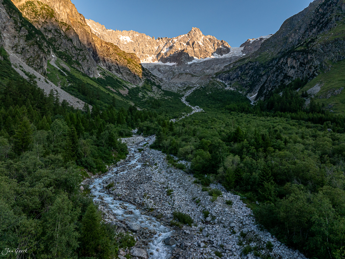 Gletschertal mit Bergbach, grünen Lärchenwäldern und schneebedecktem Gletscher im Hintergrund, Sonnenlicht auf Felswänden, Sommer im Wallis, Schweiz – Jan Geerk Fotograf Basel