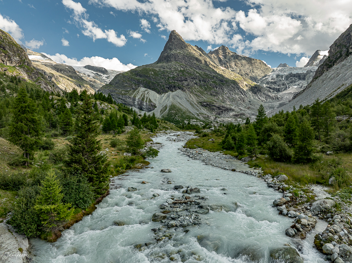 Gletscherbach im Ferret-Tal mit schneebedeckten Alpengipfeln und Lärchenwäldern, Sommerliche Alpenszenerie in der Schweiz – Jan Geerk Fotograf Basel