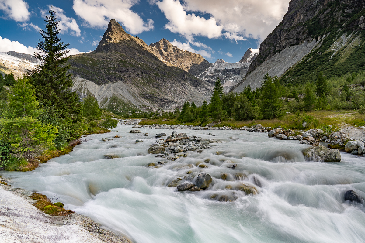 Gletscherbach im Ferret-Tal mit alpinen Lärchen, Berggipfel und Gletscher im Sommer, Wallis Schweiz – Jan Geerk Fotograf Basel