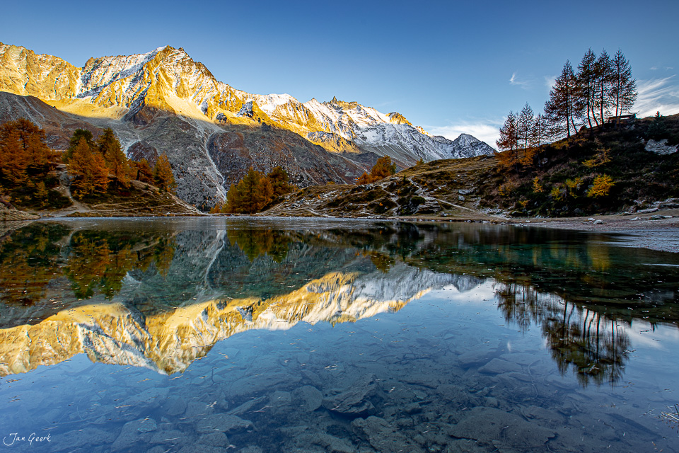 Spiegelung des Lac Bleu im Herbst mit schneebedeckten Bergen und Lärchen, Wallis, Schweiz – Jan Geerk Fotograf Basel
