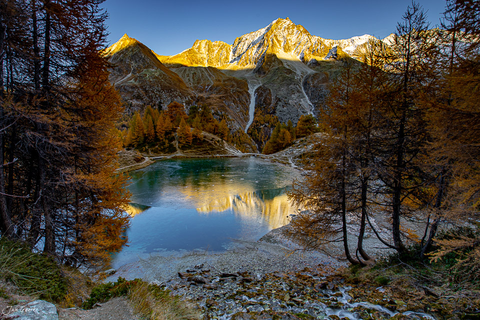 Alpensee mit Lärchen im Herbst, schneebedeckte Gipfel spiegeln sich im klaren Wasser, Val d'Herens Wallis Schweiz Jan Geerk Fotograf Basel