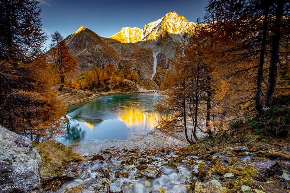 Alpensee mit Lärchen im Herbst, schneebedeckte Berggipfel spiegeln sich im klaren Wasser, Wallis Schweiz – Jan Geerk Fotograf Basel
