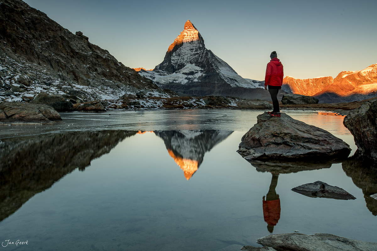 Wanderin in roter Jacke am Riffelsee mit Matterhorn-Spiegelung bei Sonnenaufgang, Wallis, Schweiz – Jan Geerk Fotograf Basel