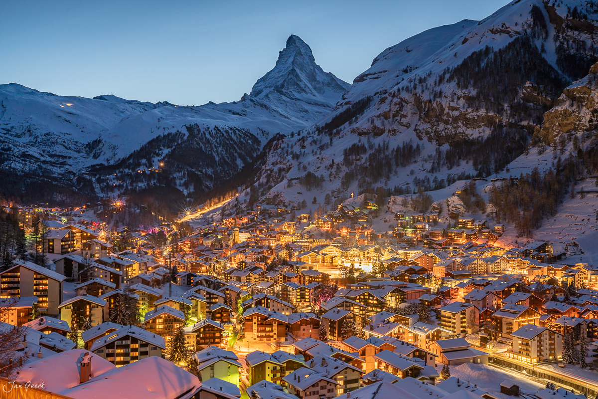 Verschneites Dorf Zermatt mit beleuchteten Häusern in Winternacht, Matterhorn im Hintergrund, Wallis Schweiz – Jan Geerk Fotograf Basel