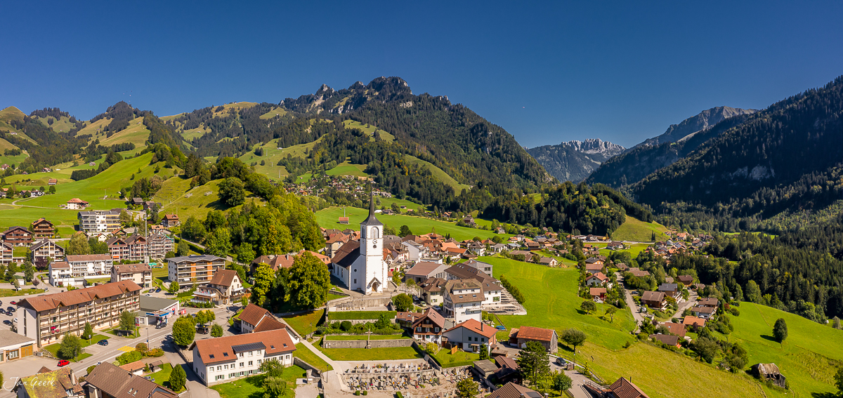 Luftaufnahme Dorf Charmey mit Kirche, grüne Berglandschaft, Sommerlicht, Westschweiz – Jan Geerk Fotograf Basel