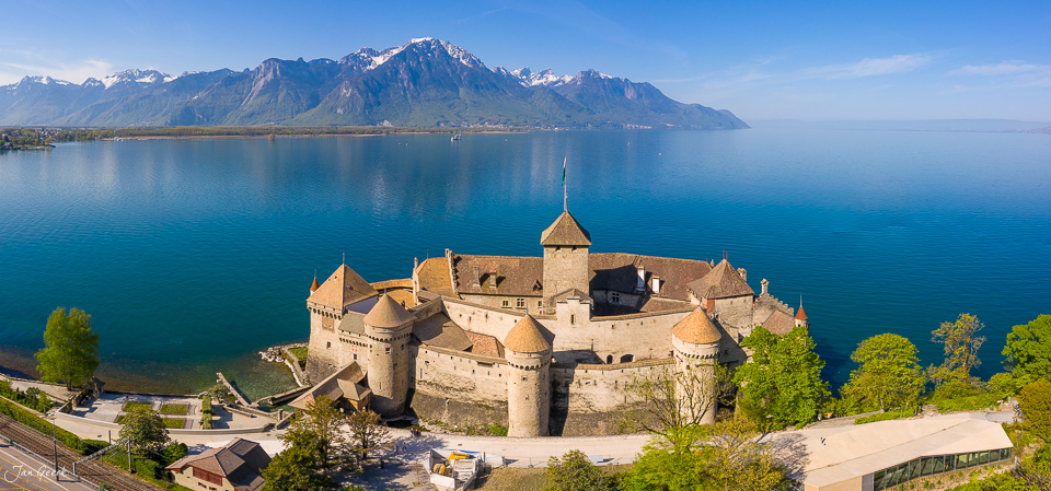 Schloss Chillon am Genfersee mit schneebedeckten Alpen im Frühlingslicht, Luftaufnahme Schweiz – Jan Geerk Fotograf Basel