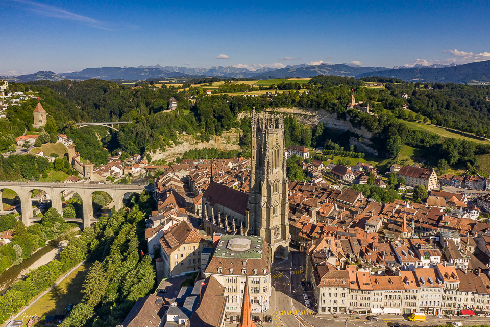 Luftaufnahme der Altstadt Fribourg mit Kathedrale Saint-Nicolas, grüne Landschaft und Alpen im Hintergrund, Sommer in der Schweiz – Jan Geerk Fotograf Basel