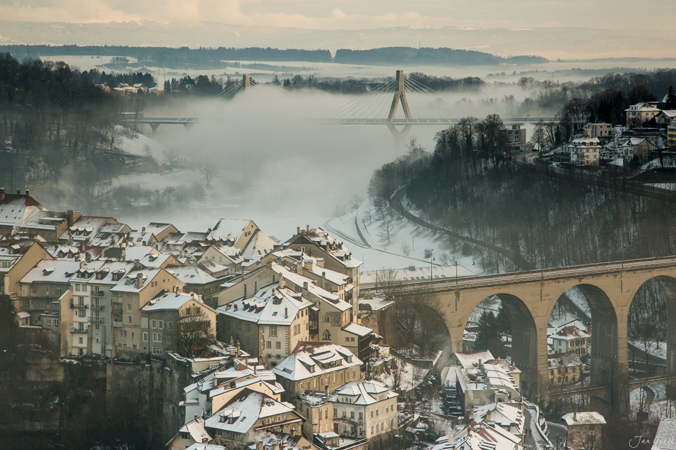 Winterliche Altstadt mit Viadukt über nebligem Tal in Fribourg, schneebedeckte Dächer und Flusslandschaft, Westschweiz – Jan Geerk Fotograf Basel