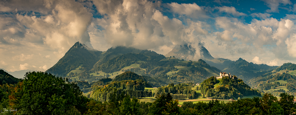 Panoramablick auf Greyerz mit Bergen, grünen Hügeln und Schloss in Sommerlicht, Westschweiz – Jan Geerk Fotograf Basel