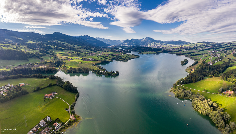 Luftaufnahme des Lac de la Gruyère mit grünen Uferlandschaften und Alpenpanorama, Sommer, Westschweiz – Jan Geerk Fotograf Basel