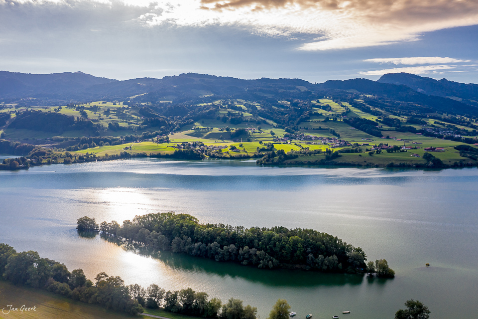 Luftaufnahme Lac de la Gruyère mit bewaldeter Insel, grüne Hügel und Berge in goldenem Kantlicht, Westschweiz – Jan Geerk Fotograf Basel