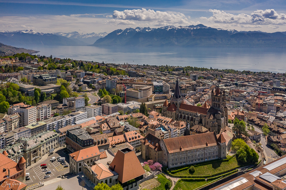 Luftaufnahme der Stadt Lausanne mit Kathedrale, Genfersee und schneebedeckten Alpen im Frühling – Jan Geerk Fotograf Basel Schweiz