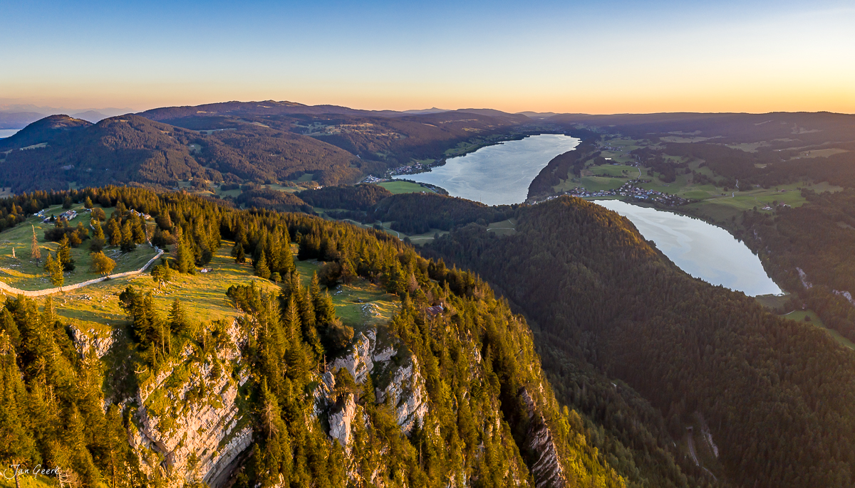 Luftaufnahme der Vallée de Joux mit zwei Seen, Nadelwäldern und Felsformationen im goldenen Sommerlicht, Jura Schweiz – Jan Geerk Fotograf Basel