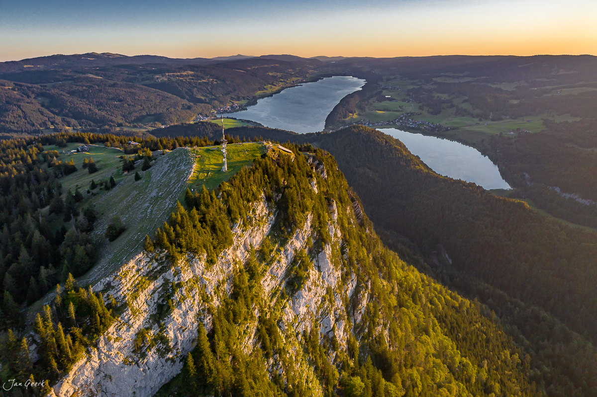 Dramatische Luftaufnahme der Vallée de Joux mit zwei Seen, Felsklippe und Nadelwald im Sommerlicht, Schweiz – Jan Geerk Fotograf Basel
