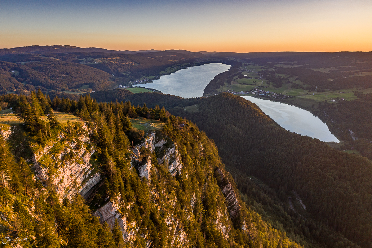 Luftaufnahme Vallée de Joux mit zwei Seen, Felsvorsprung und Fichtenwäldern in goldener Sommerstimmung, Jura, Schweiz – Jan Geerk Fotograf Basel