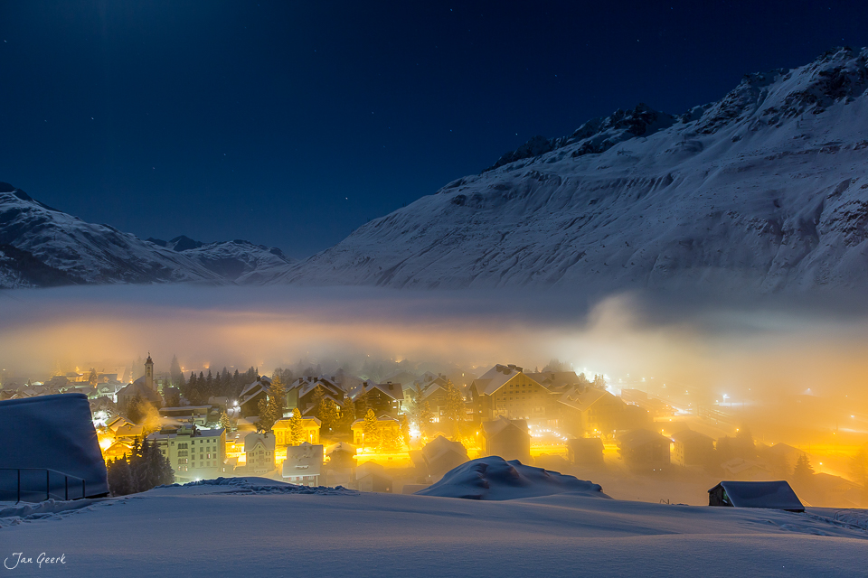 Verschneite Berglandschaft mit beleuchteter Siedlung bei Nacht in Andermatt, Zentralschweiz – Jan Geerk Fotograf Basel