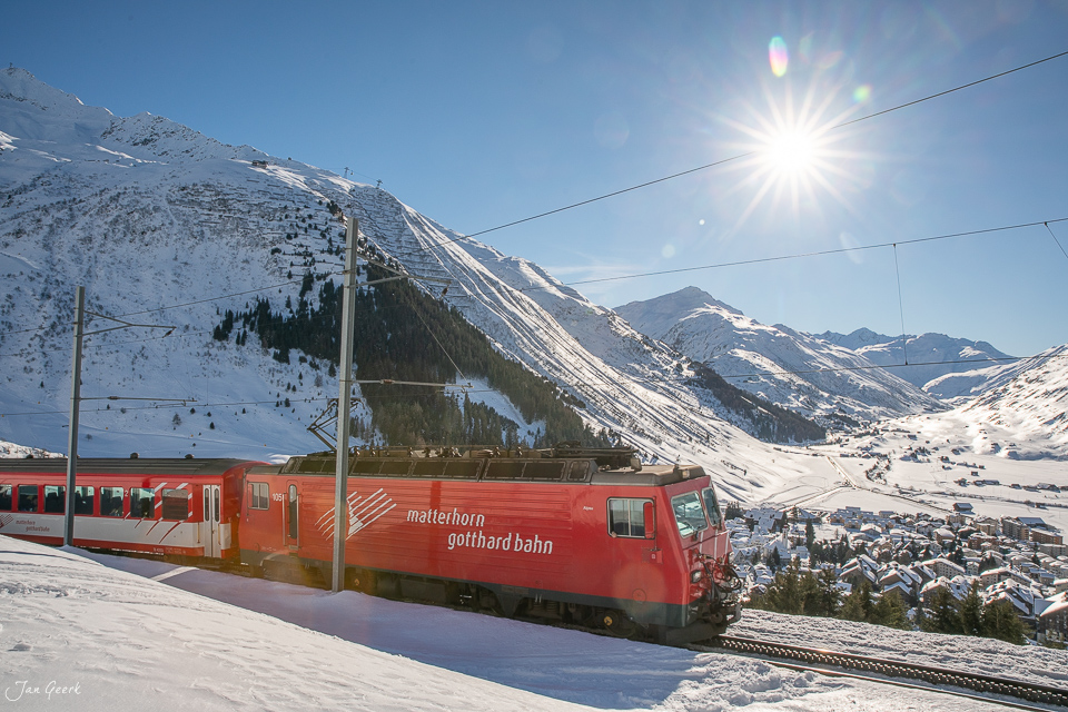 Rote Gotthardbahn mit schneebedeckten Bergen bei Andermatt im Winter, Schweiz – Jan Geerk Fotograf Basel
