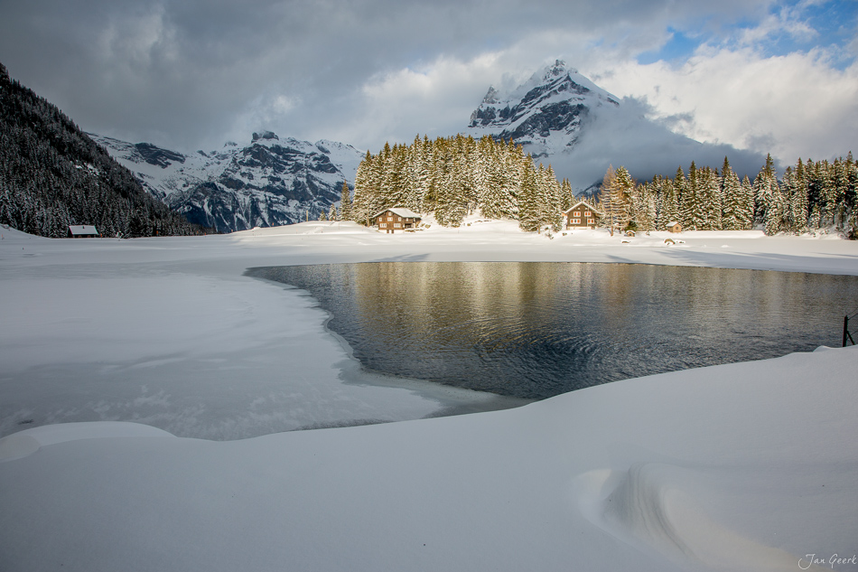 Gefrorener Arnisee mit schneebedeckten Bergen und Berghütten im Winter, Zentralschweiz – Jan Geerk Fotograf Basel