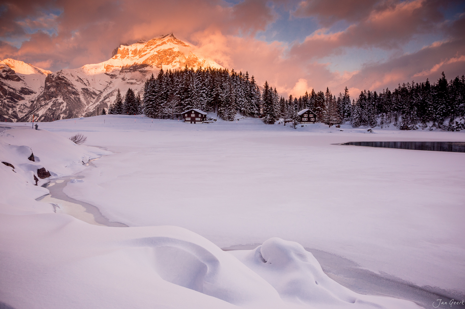 Gefrorener Arnisee im Winter mit verschneiter Landschaft, Berghütten und schneebedecktem Berg bei Sonnenaufgang in der Zentralschweiz – Jan Geerk Fotograf Basel
