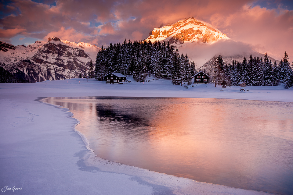Gefrorener Arnisee im Winter mit schneebedeckten Bergen und Berghütten bei Sonnenuntergang in der Schweiz – Jan Geerk Fotograf Basel