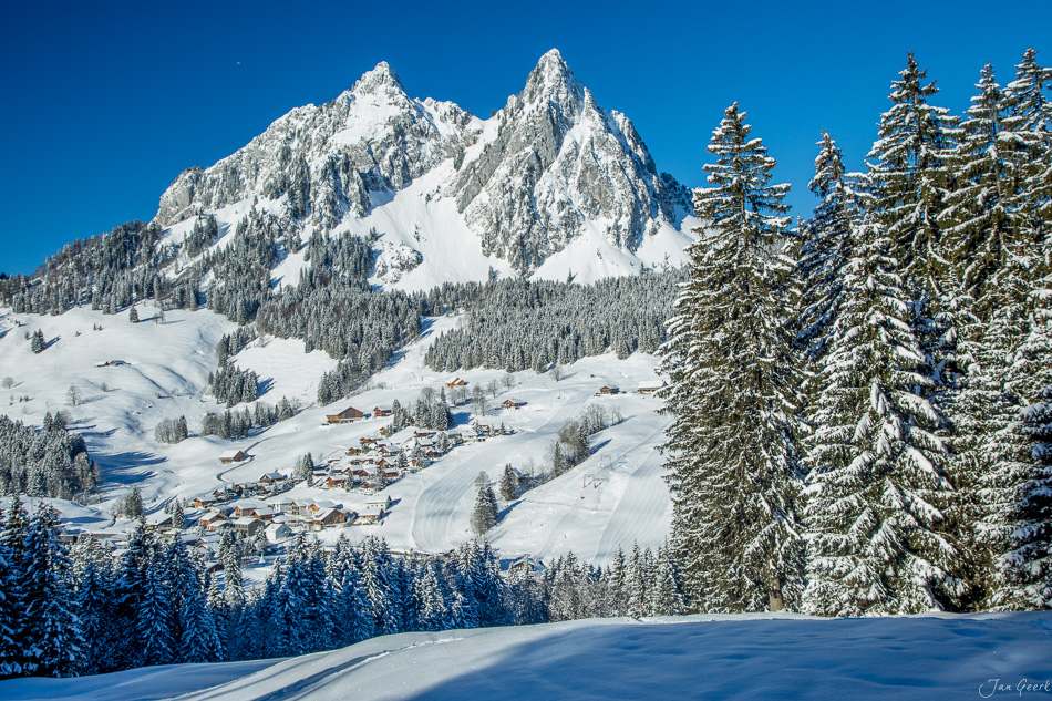 Schneebedeckte Berglandschaft mit Mythen Brunni Dorf und verschneiten Fichten Winter Zentralschweiz Schweiz – Jan Geerk Fotograf Basel