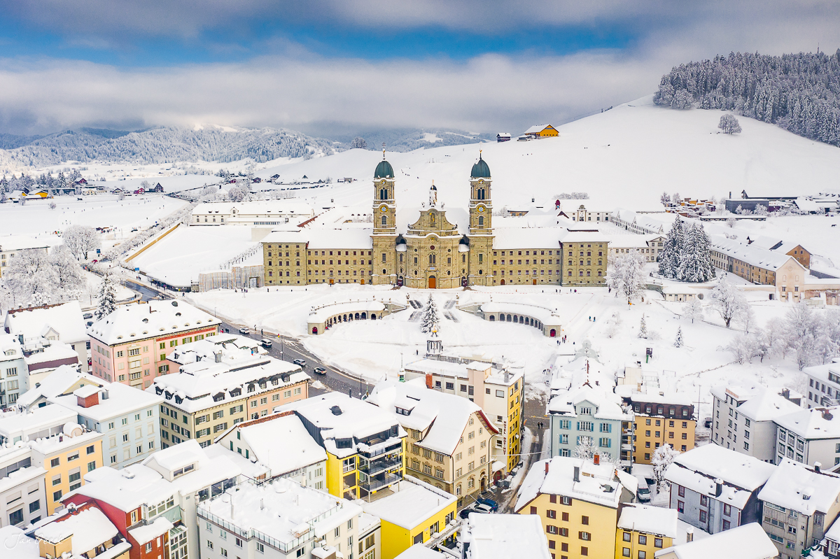 Kloster Einsiedeln im Schnee mit verschneiter Berglandschaft im Winter, Luftaufnahme Schweiz – Jan Geerk Fotograf Basel