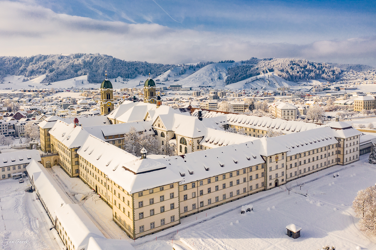 Kloster Einsiedeln im Schnee, Luftaufnahme mit verschneiten Dächern und Bergpanorama, Winter in der Schweiz – Jan Geerk Fotograf Basel