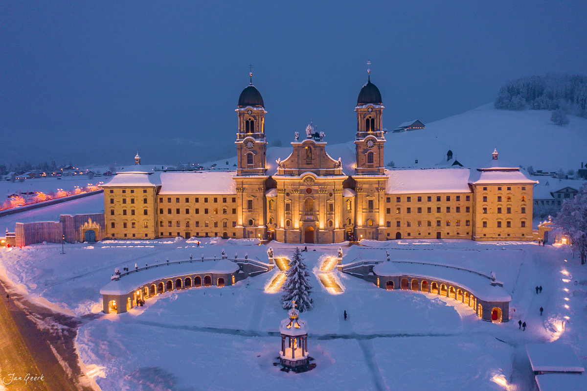 Kloster Einsiedeln schneebedeckt bei Dämmerung mit beleuchteter Barockfassade und gefrorenem See, Zentralschweiz – Jan Geerk Fotograf Basel