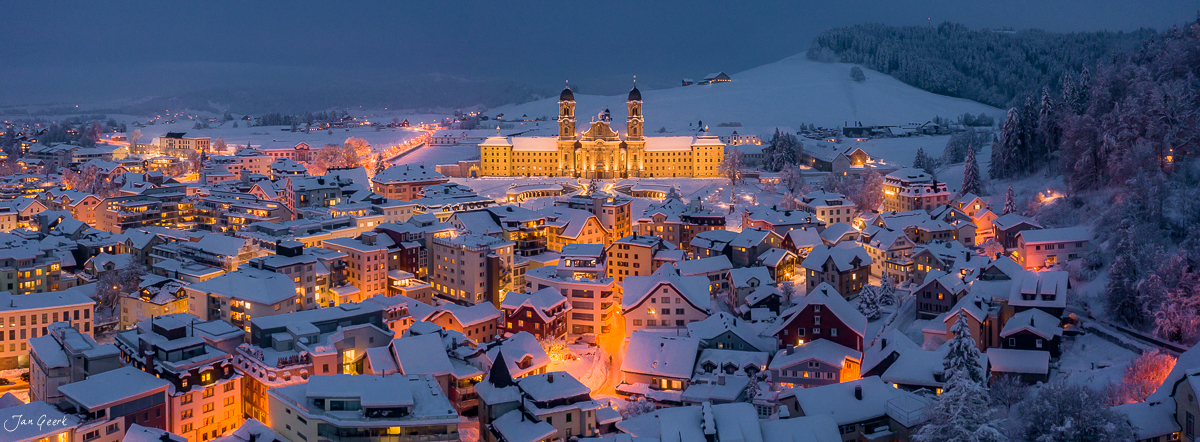 Kloster Einsiedeln im Schnee bei Kantlicht, Luftaufnahme der Klosteranlage mit schneebedecktem Dorf im Winter, Zentralschweiz – Jan Geerk Fotograf Basel