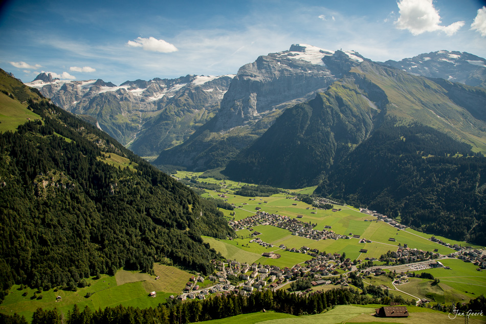 Luftaufnahme des Engelberg Tals mit grünen Wiesen, verschneiten Gipfeln und traditionellen Häusern im Sommer in der Zentralschweiz – Jan Geerk Fotograf Basel