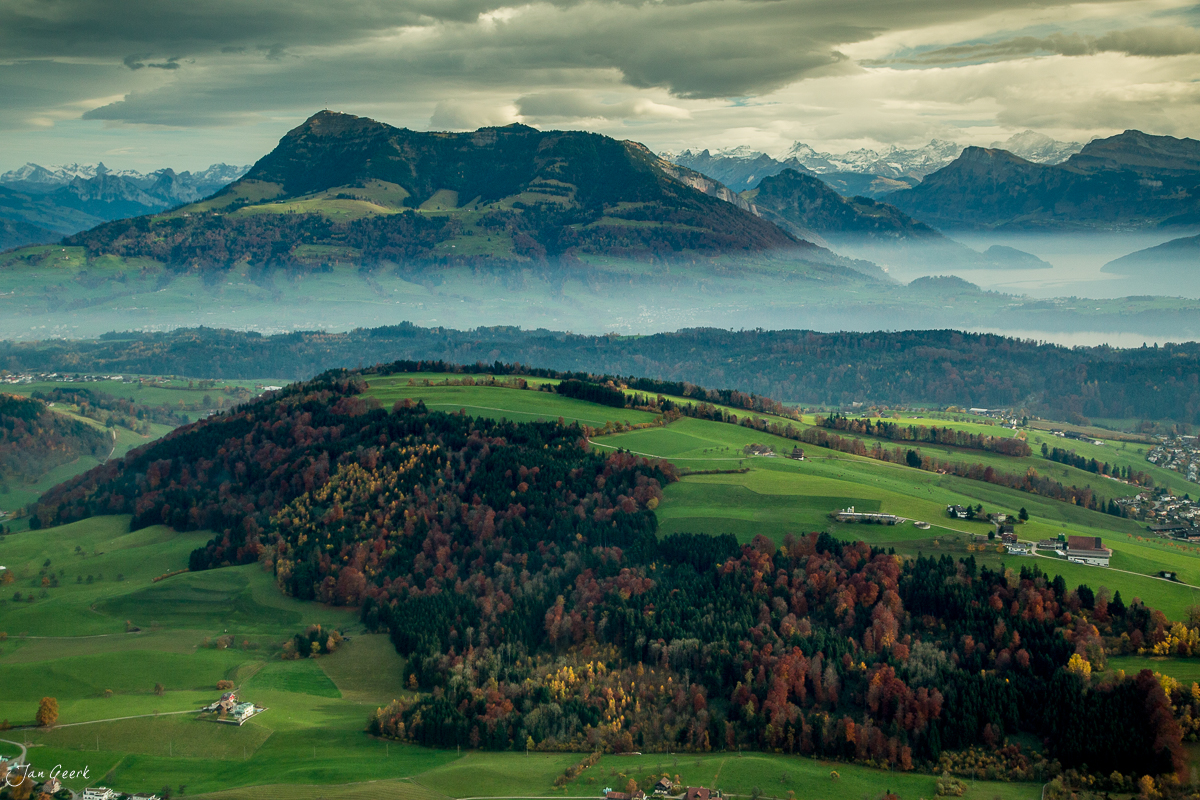Luftaufnahme des Honegg mit Herbstwald, grünen Wiesen und Alpensilhouette in der Zentralschweiz – Jan Geerk Fotograf Basel