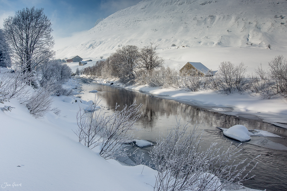 Winterlandschaft Hospental mit gefrorenem Bach, schneebedeckten Bergen und traditionellen Häusern, Zentralschweiz Schweiz – Jan Geerk Fotograf Basel