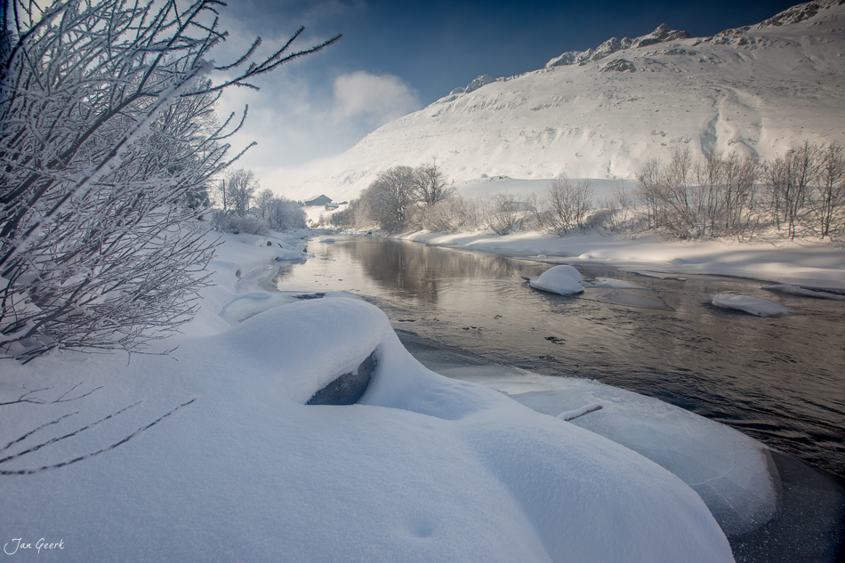 Winterlicher Fluss mit verschneiten Ufern und gefrorenen Ästen am Oberalppass, Zentralschweiz Schweiz – Jan Geerk Fotograf Basel