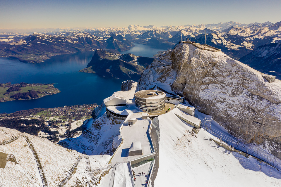 Luftaufnahme des schneebedeckten Pilatus mit modernem Besucherzentrum, Vierwaldstättersee und Alpen im Winter, Zentralschweiz – Jan Geerk Fotograf Basel