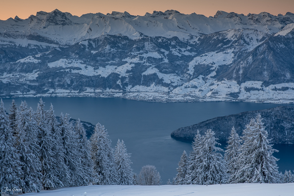 Schneebedeckte Lärchen und Bergsee im Winter auf der Rigi, dahinter verschneite Alpenlandschaft bei Sonnenaufgang, Zentralschweiz Schweiz – Jan Geerk Fotograf Basel