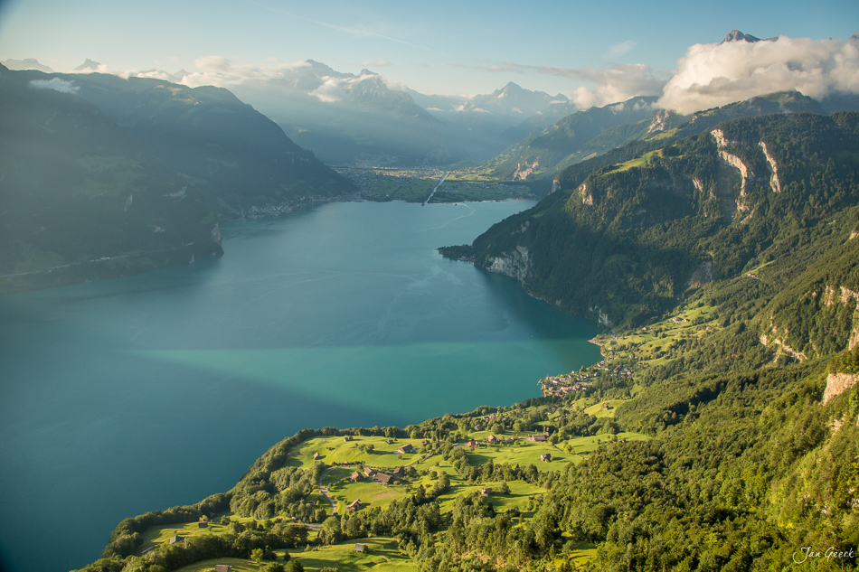 Luftaufnahme des Vierwaldstättersees bei Seelisberg mit grünen Alpenweiden, Wäldern und schneebedeckten Bergen im Sommer – Jan Geerk Fotograf Basel