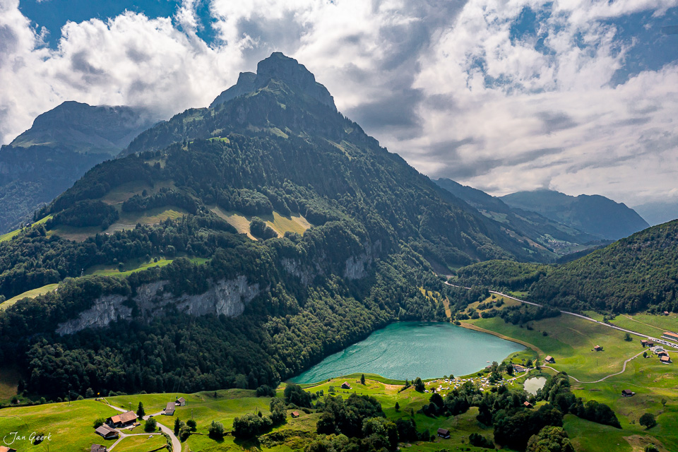 Luftaufnahme des türkisblauen Treib-Sees umgeben von grünen Wiesen, bewaldeten Bergen und einem markanten Felsgipfel im Sommer in der Zentralschweiz – Jan Geerk Fotograf Basel