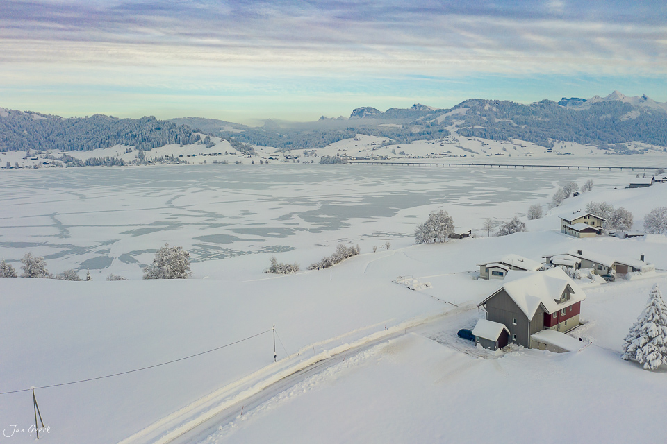 Winterliche Luftaufnahme des Sihlsee mit schneebedeckten Uferhäusern und gefrorener Seefläche, Kantlicht am Morgen, Zentralschweiz – Jan Geerk Fotograf Basel