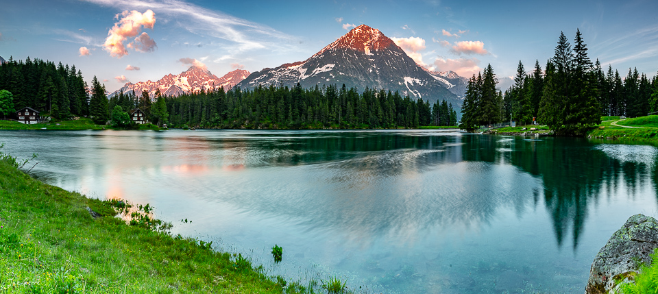 Alpiner See mit Spiegelbild des schneebedeckten Bergs, Kontrast grüner Wiesen und Nadelwald, Sommerlicht, Uri Schweiz – Jan Geerk Fotograf Basel