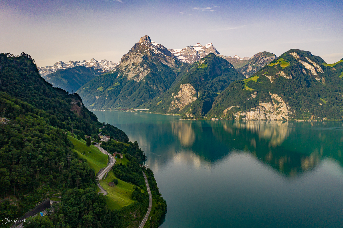 Alpensee mit Gebirgspanorama und Serpentinenstraße, grüne Wälder und Schneeberge, Sommerlicht, Zentralschweiz – Jan Geerk Fotograf Basel