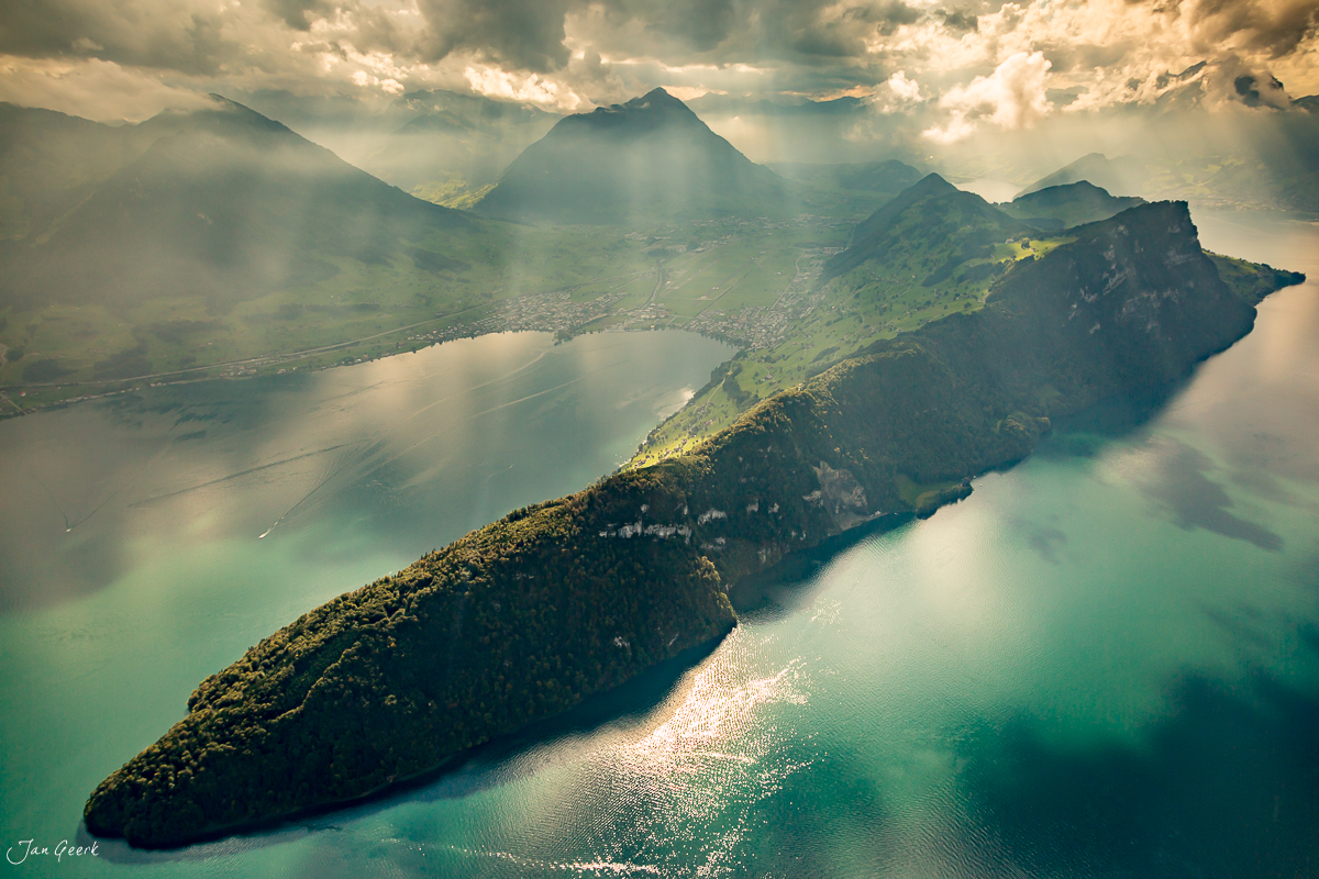 Luftaufnahme Vierwaldstättersee mit bewaldeter Halbinsel, türkisgrünes Wasser, Bergkulisse, sommerliche Lichtstimmung, Zentralschweiz – Jan Geerk Fotograf Basel