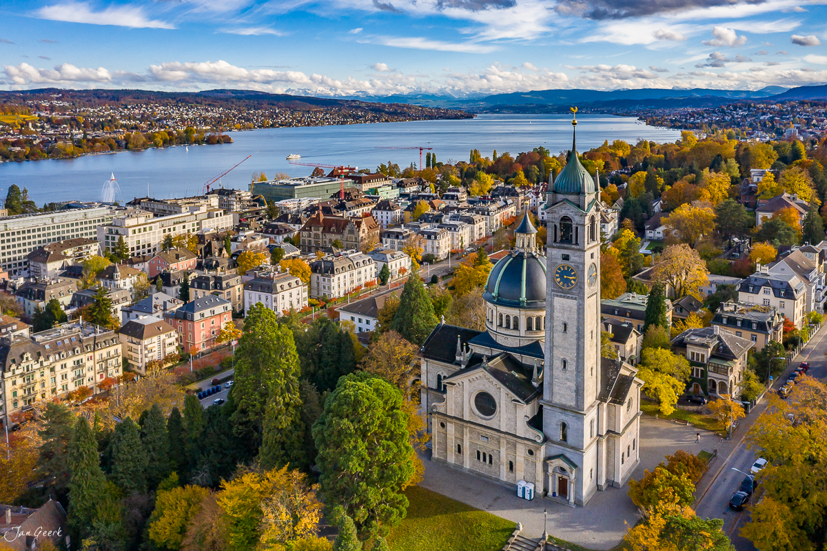 Luftaufnahme der Kirche Zürich mit Zürichsee, Herbstfarben und Alpen im Hintergrund – Jan Geerk Fotograf Basel