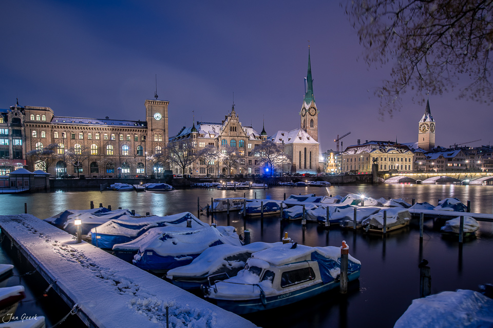 Schneebedeckte Boote im Hafen von Zürich bei Nacht mit beleuchteter Altstadt und Fraumünster Kirche, Winterstimmung Schweiz – Jan Geerk Fotograf Basel