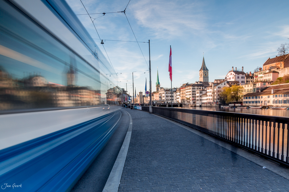 Tramvorbeifahrt an der Schipfe mit Altstadt Zürich, Limmat und Kirchtürmen im Frühlingslicht – Schweiz, Jan Geerk Fotograf Basel