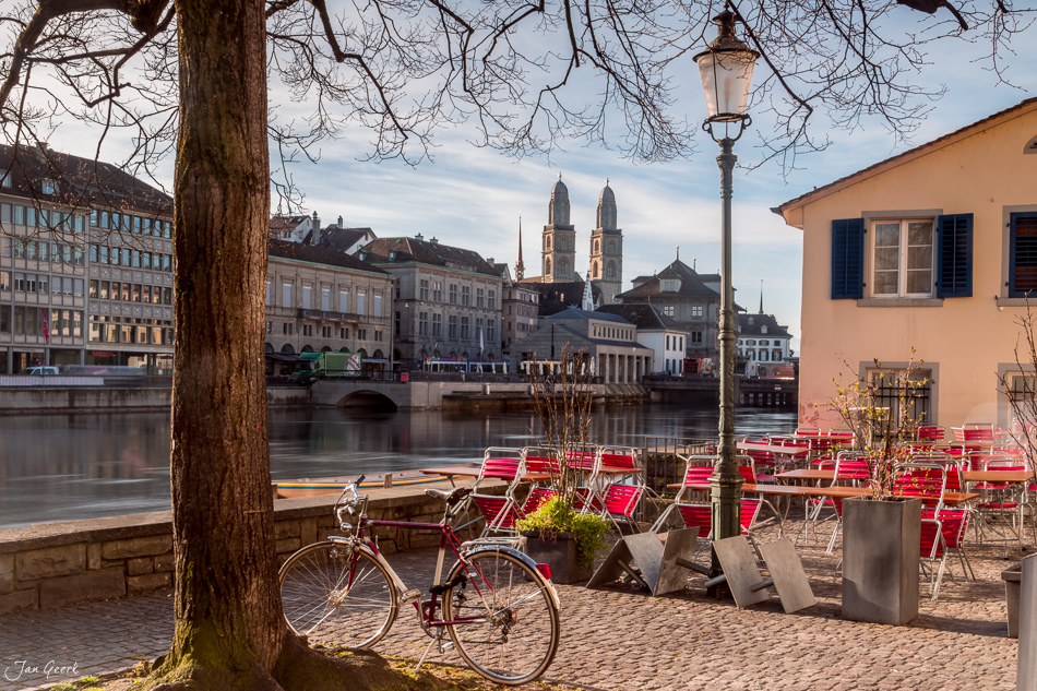 Fahrrad und rote Liegestühle an der Schipfe in Zürich, Frühjahrsszene mit Limmat und Altstadt, Schweiz – Jan Geerk Fotograf Basel